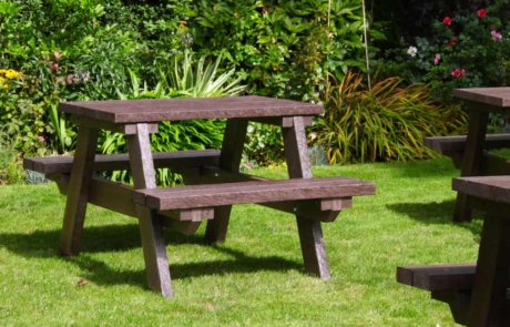 1m-Bulk-Tables-1 Small brown picnic tables set on grass by a flowerbed