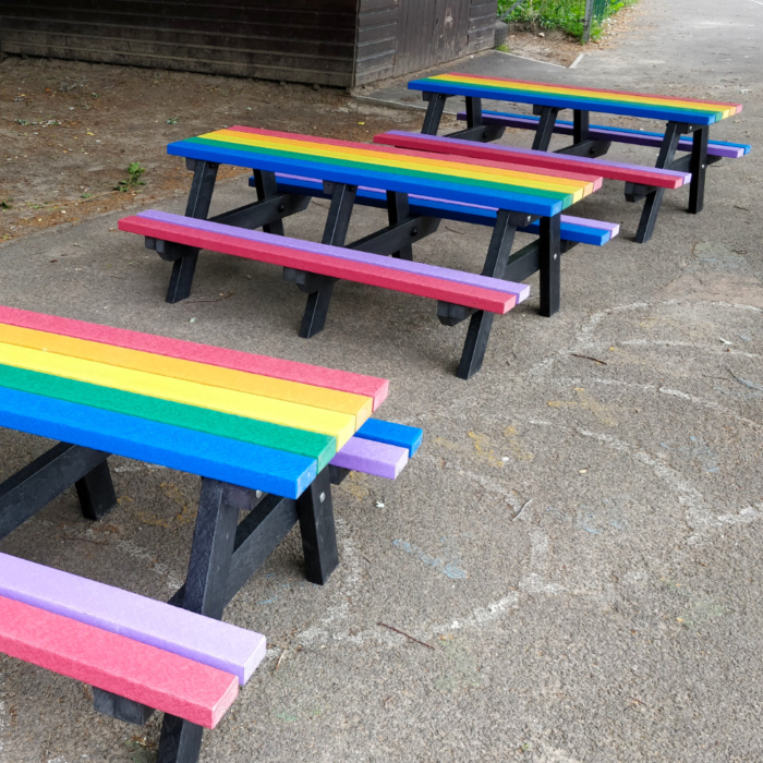 Row of three rainbow coloured childrens picnic tables in a school playground