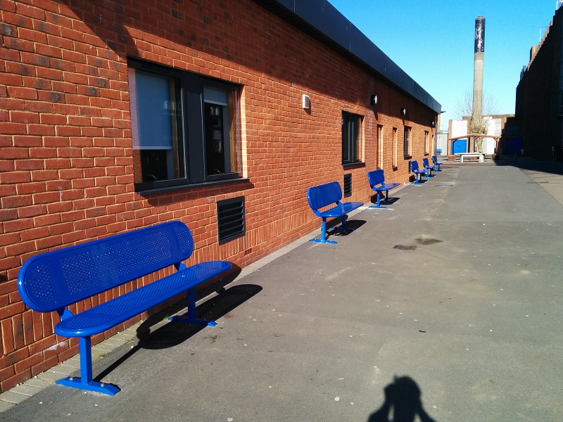 Blue steel seats lined up against a red brick building