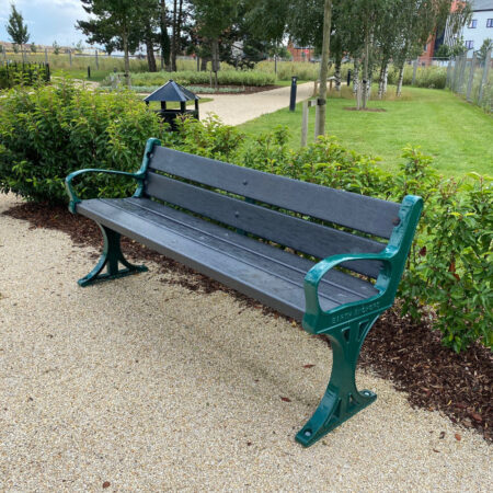 Evergreen Seat In Situ Green framed cast iron seat in a park with black recycled plastic slats.