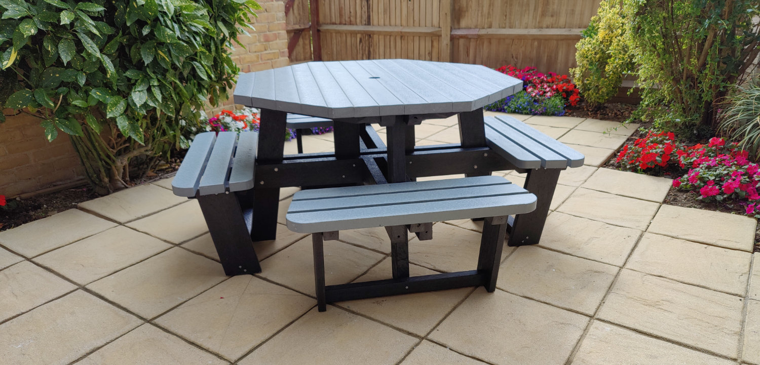 Grey and black recycled plastic picnic table on garden paving slabs