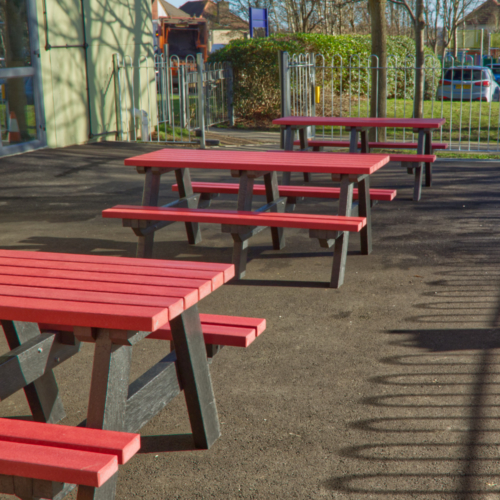 Row of red and black junior picnic tables in a school playground