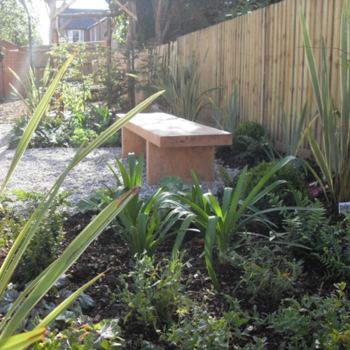 Wide oak bench by fence in garden setting