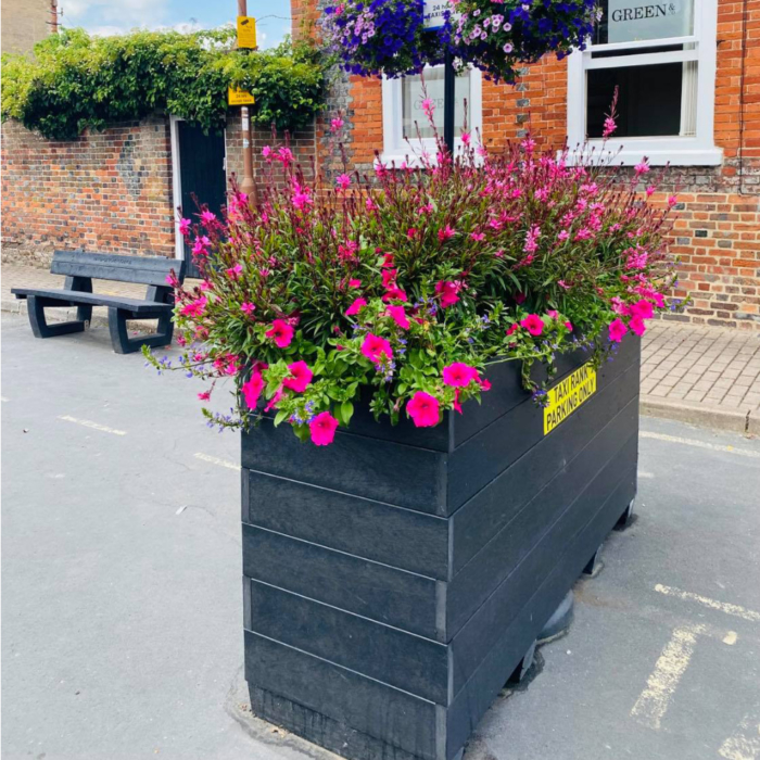 Blockade planter with a taxi rank sign on it. It is filled with pink flowers.