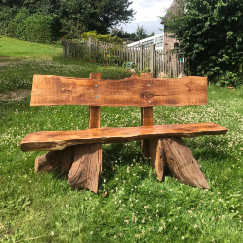 Oak seat with part tree trunk shaped legs. Set on grass,