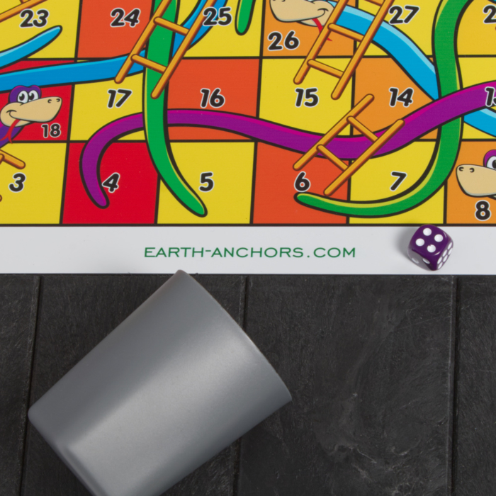 Partial picture of a snakes and ladder game board with a purple dice and grey dice tumbler
