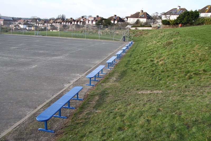 Steel benches in a row next to a grass verge in a school playground