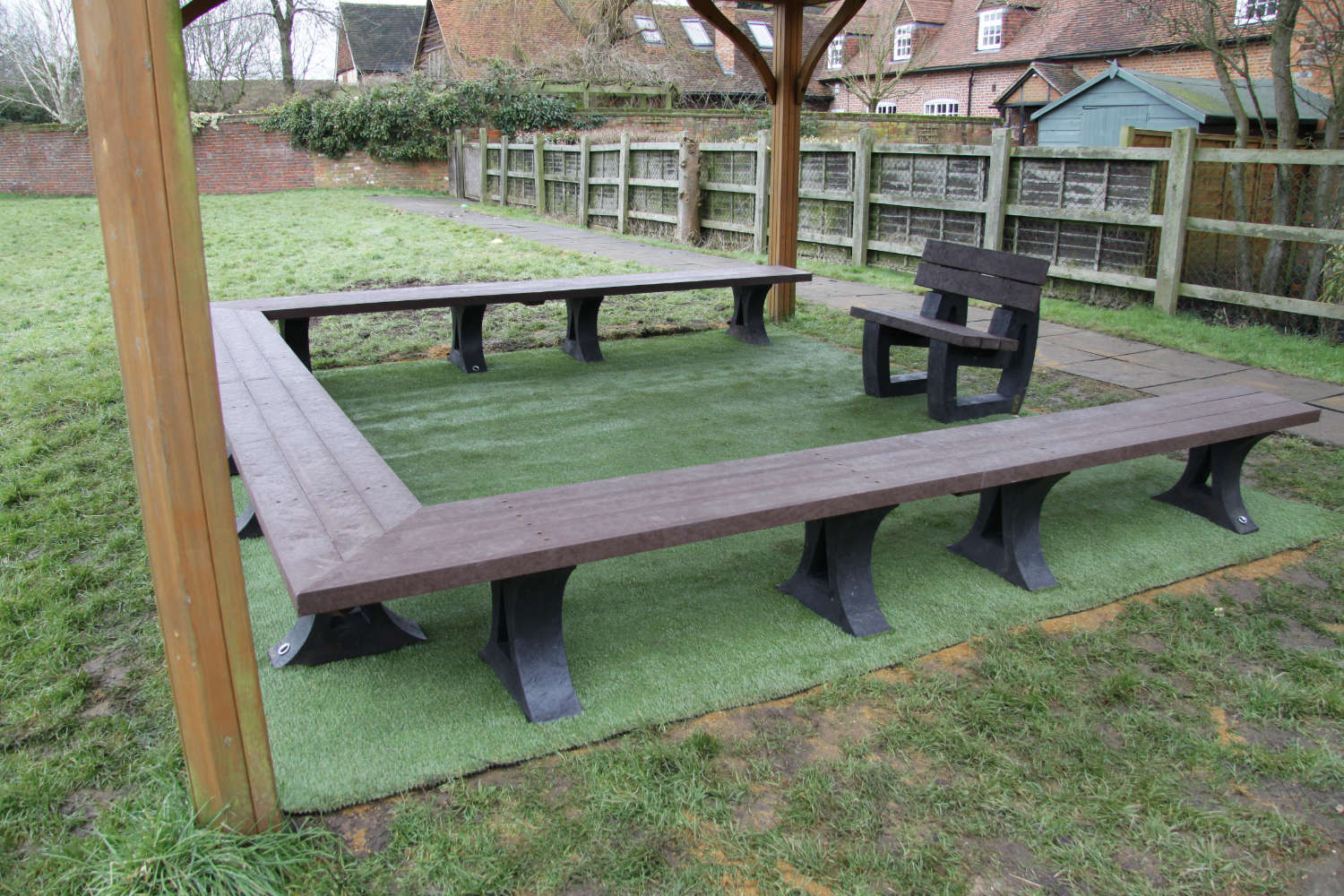 Recycled plastic benches arranged in an open square shape with a seat on the fourth side. Set on artificial grass.